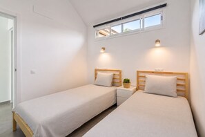 Un dormitorio con dos camas individuales, una mesita de noche pequeña con una planta y una ventana sobre las camas.