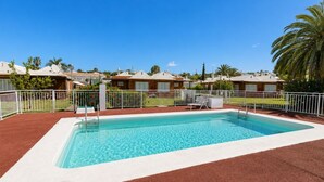 A rectangular swimming pool with a white border, surrounded by a white fence, and a red ground cover. - GuestReady - Melocotones Family Bungalow (San Bartolomé de Tirajana)