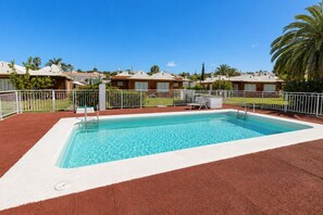 Una piscina rectangular con borde blanco, rodeada por una valla blanca y un suelo cubierto de rojo.