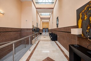 Eine Hotelhalle mit Marmorboden, einer Rezeption, einer Sitzecke und einem großen abstrakten Gemälde an der Wand.