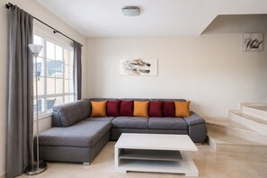 Ein modernes Wohnzimmer mit einem grauen Ecksofa, einem weißen Couchtisch und einer Treppe, die zu einer oberen Etage führt.