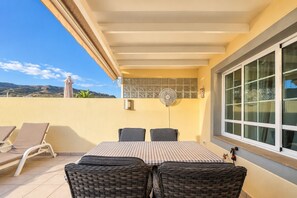 Eine Terrasse mit Tisch, Stühlen, einem Ventilator und Blick auf die Hügel.