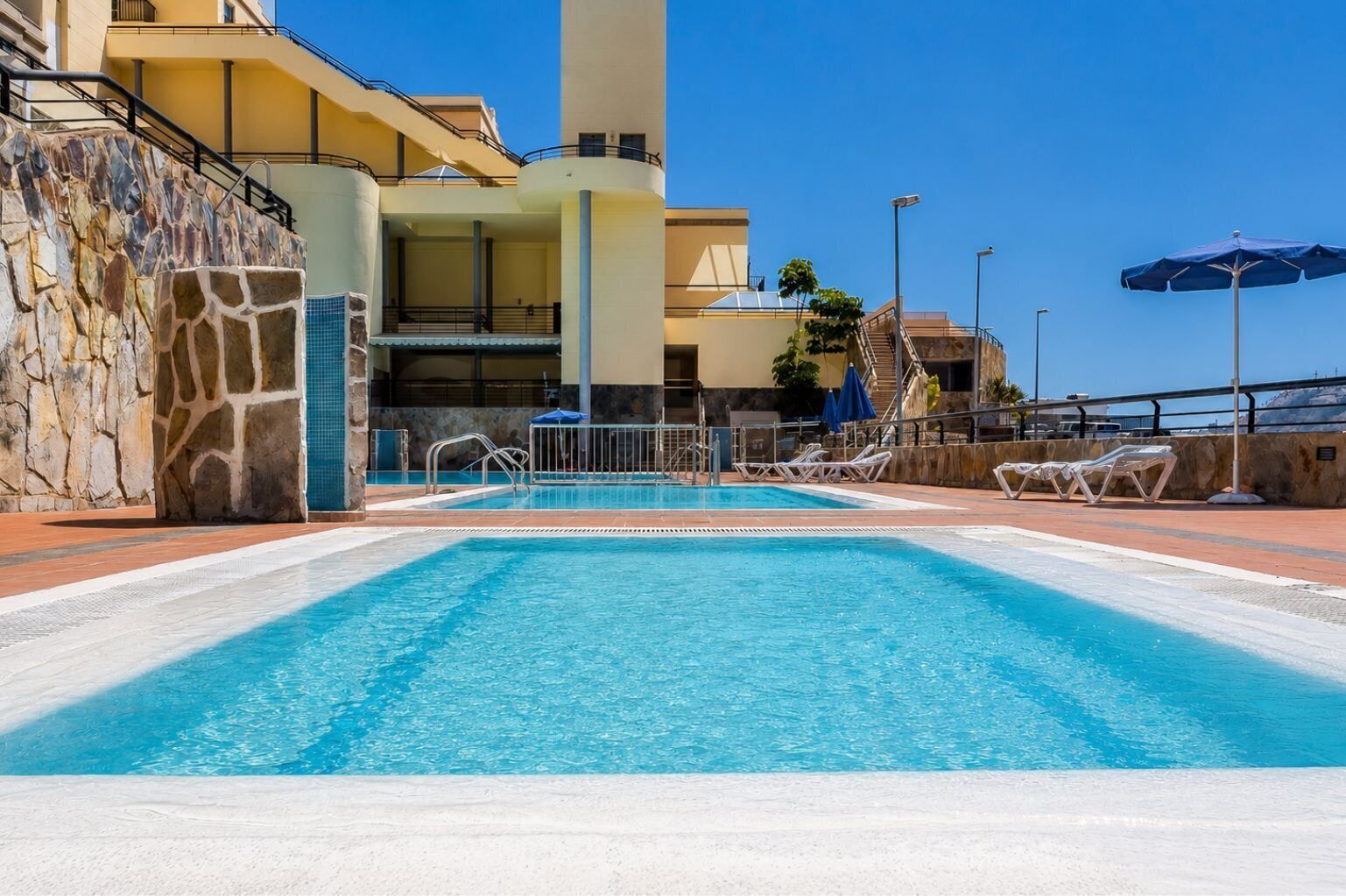 Una piscina con sillones de descanso y un muro de piedra.