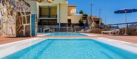 Una piscina con sillones de descanso y un muro de piedra.