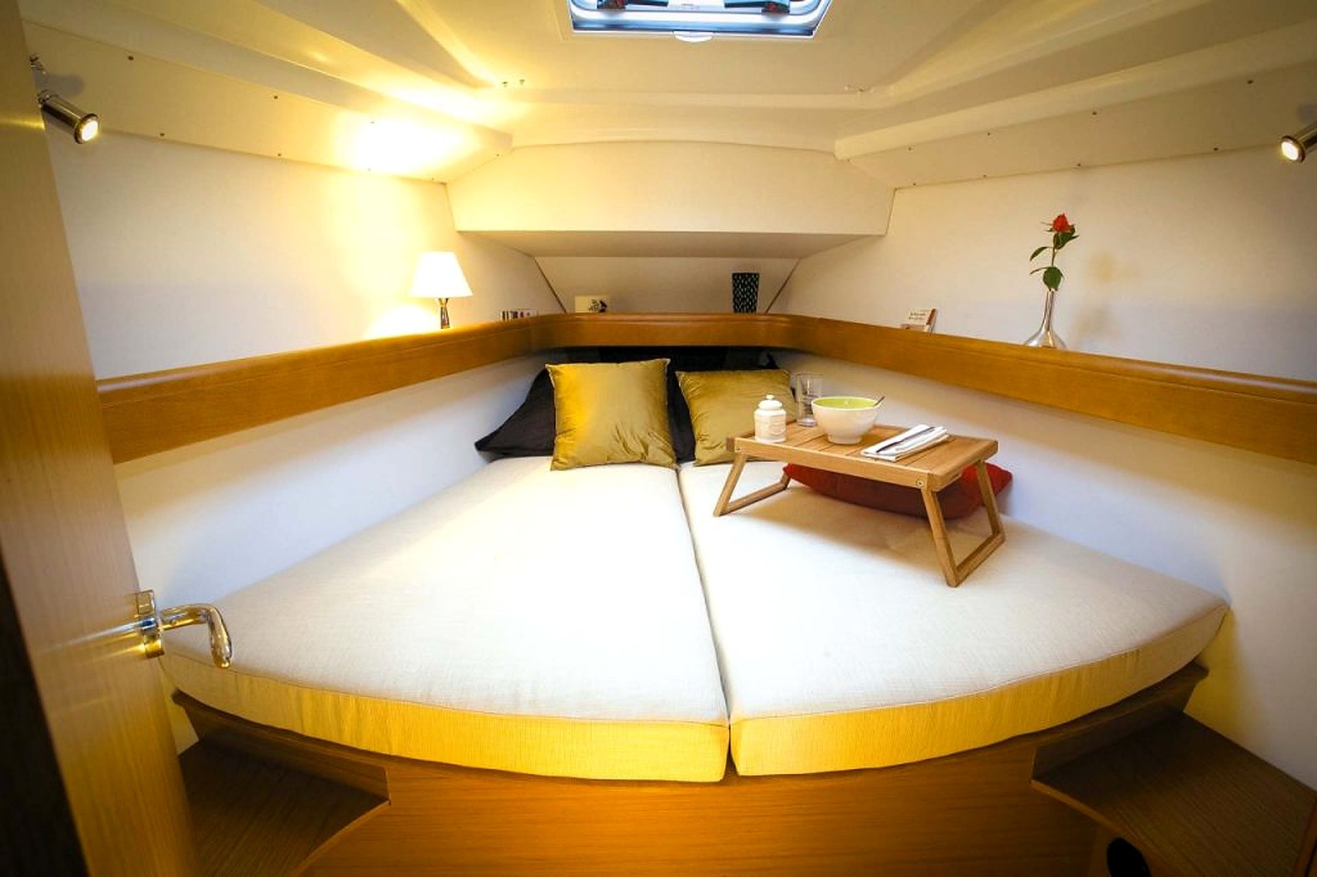 A circular bed with a wooden frame, a bedside table with a book and a glass, and a single red rose on the wall.