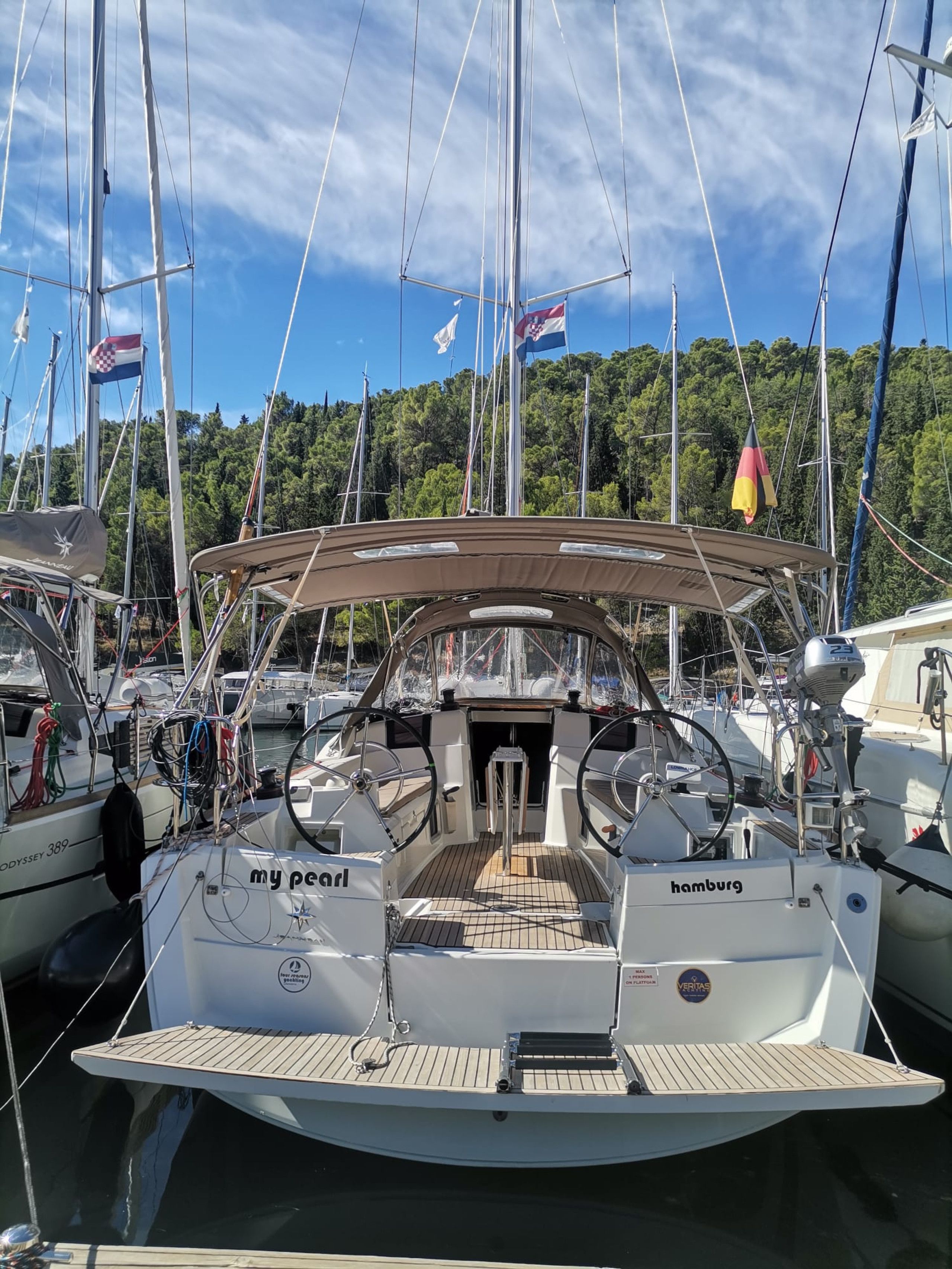 Eine Segelyacht liegt in einer Marina festgemacht, mit mehreren Flaggen, einem Steuerrad und einer Kabine mit dem Namen 'my petal'.