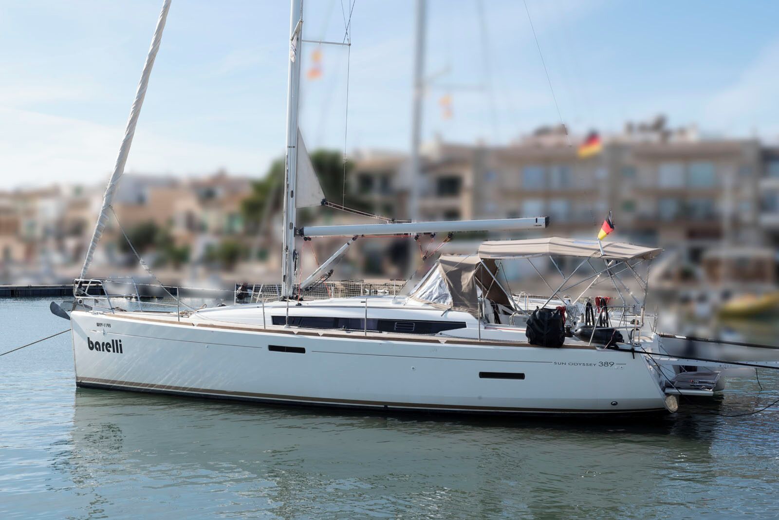 Un velero llamado 'barelli' atracado en un puerto deportivo con un paisaje urbano al fondo.