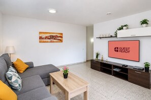 Moderni olohuone, jossa on sohva, sohvapöytä, litteänäyttöinen televisio ja taulu seinällä.