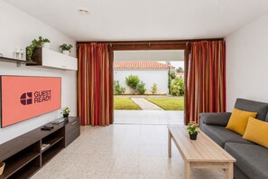 Ein modernes Wohnzimmer mit Flachbildfernseher, einer Couch, einem Couchtisch und einer Glastür zum Garten.