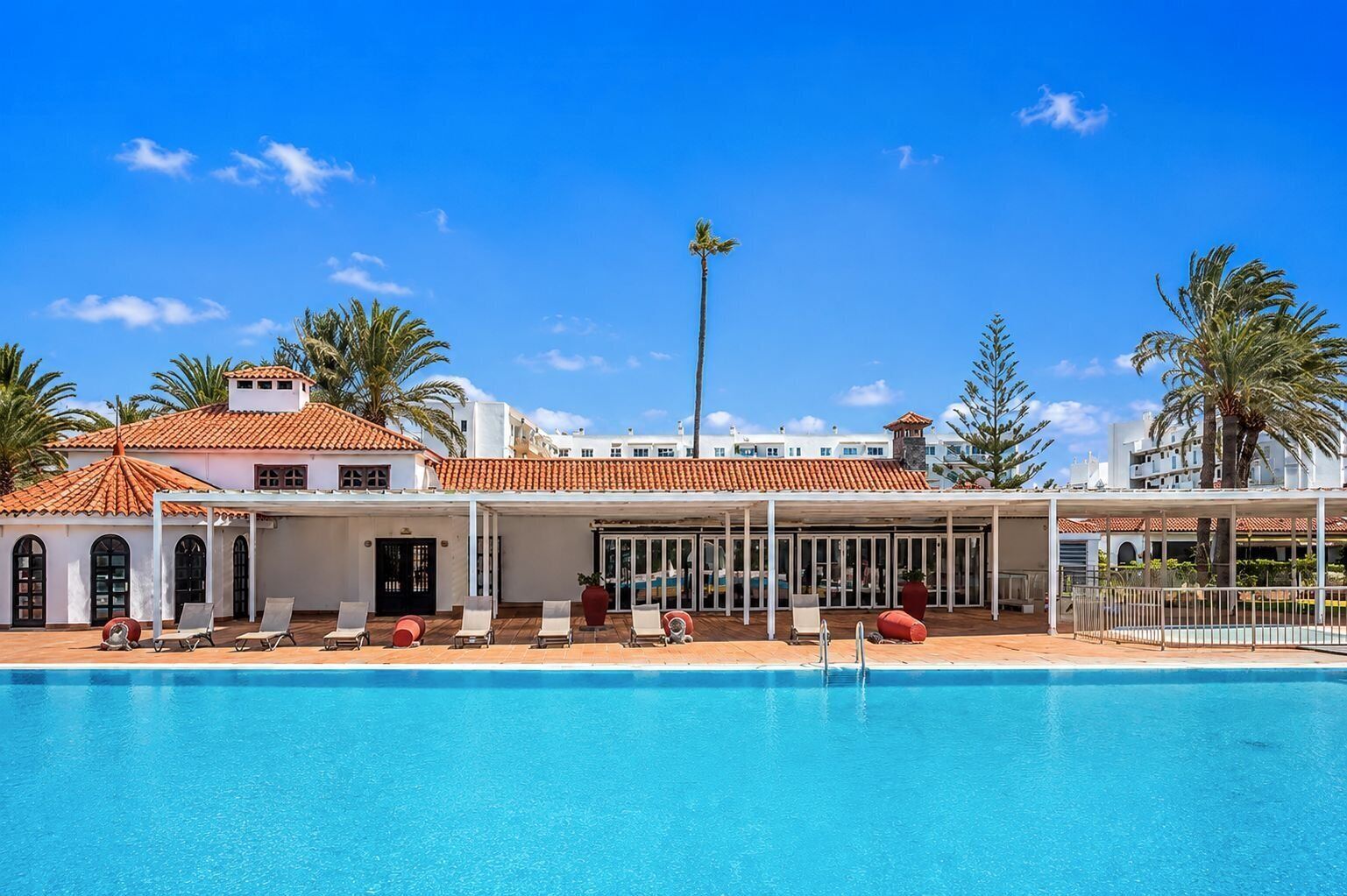 Um hotel com piscina, espreguiçadeiras e palmeiras.