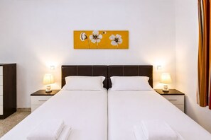 Ein Doppelbett mit weißen Laken, zwei Nachttische mit Lampen, ein Wandbild mit Blumen und ein dunkles Kopfstück.