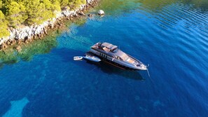 A large yacht anchored in clear blue waters with a rocky shoreline and dense greenery in the background. - Sun-Kissed Sailing Adventure in Split, Croatia (Split)