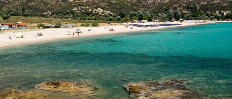 Uma praia com águas turquesa cristalinas, margens rochosas e um cenário montanhoso.