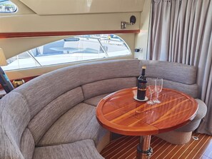 A curved seating area with a round wooden table, a bottle, and two glasses. - Sun-Kissed Sailing Adventure in Islas Baleares, Mallorca (Andratx)
