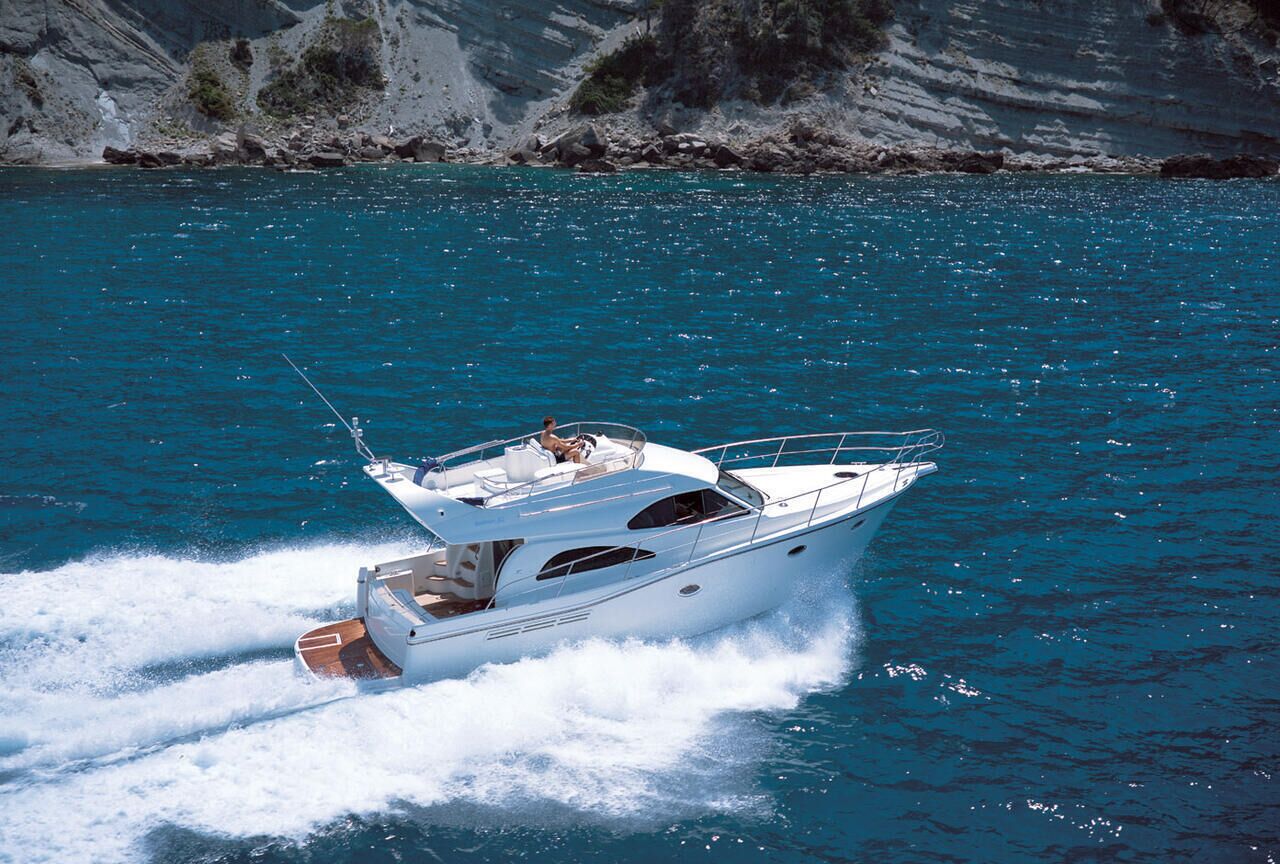A yacht on a body of water with rocky cliffs in the background.
