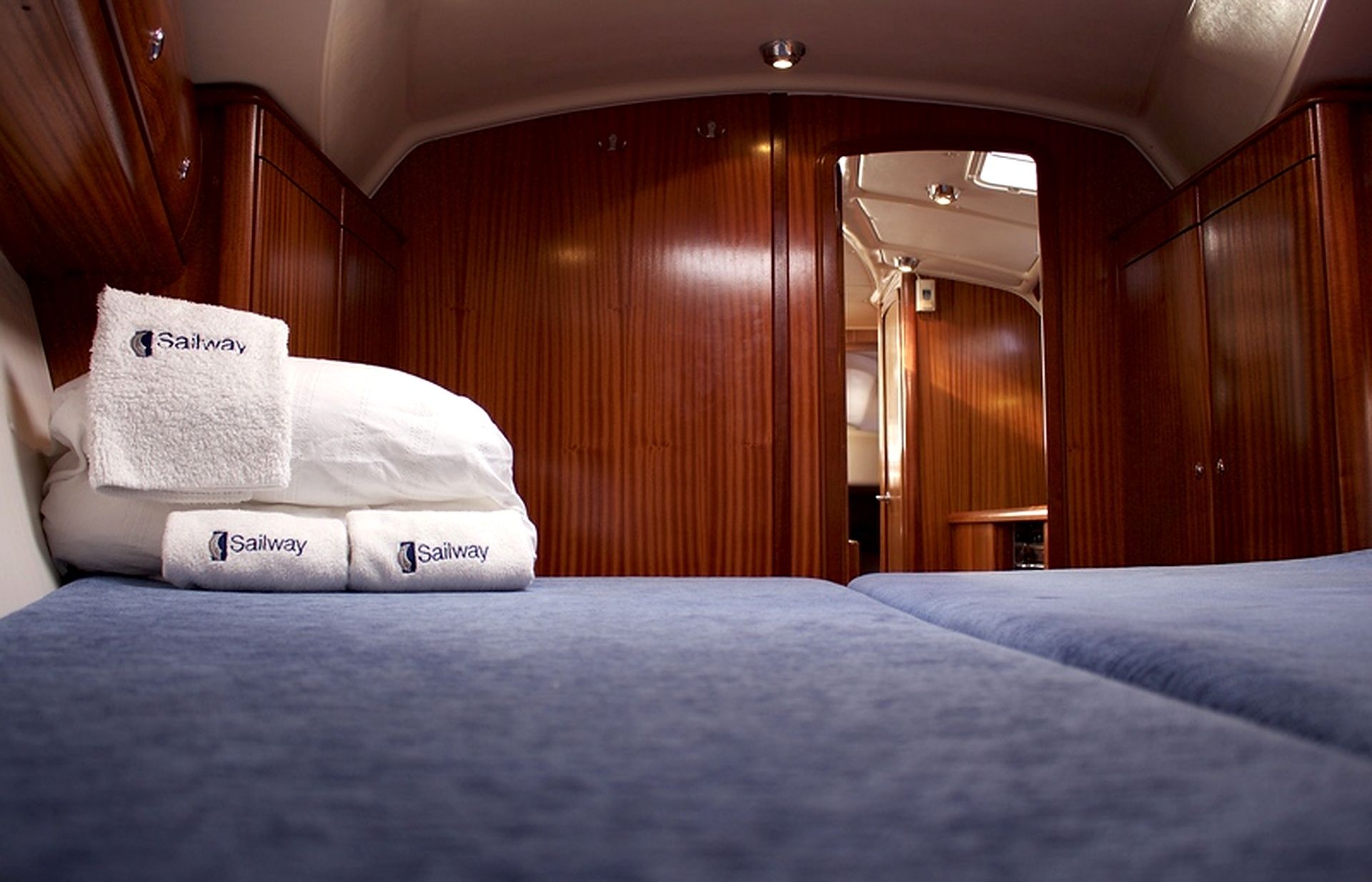 A cabin with wooden walls, a bed with blue bedding, and a set of white towels with a logo.