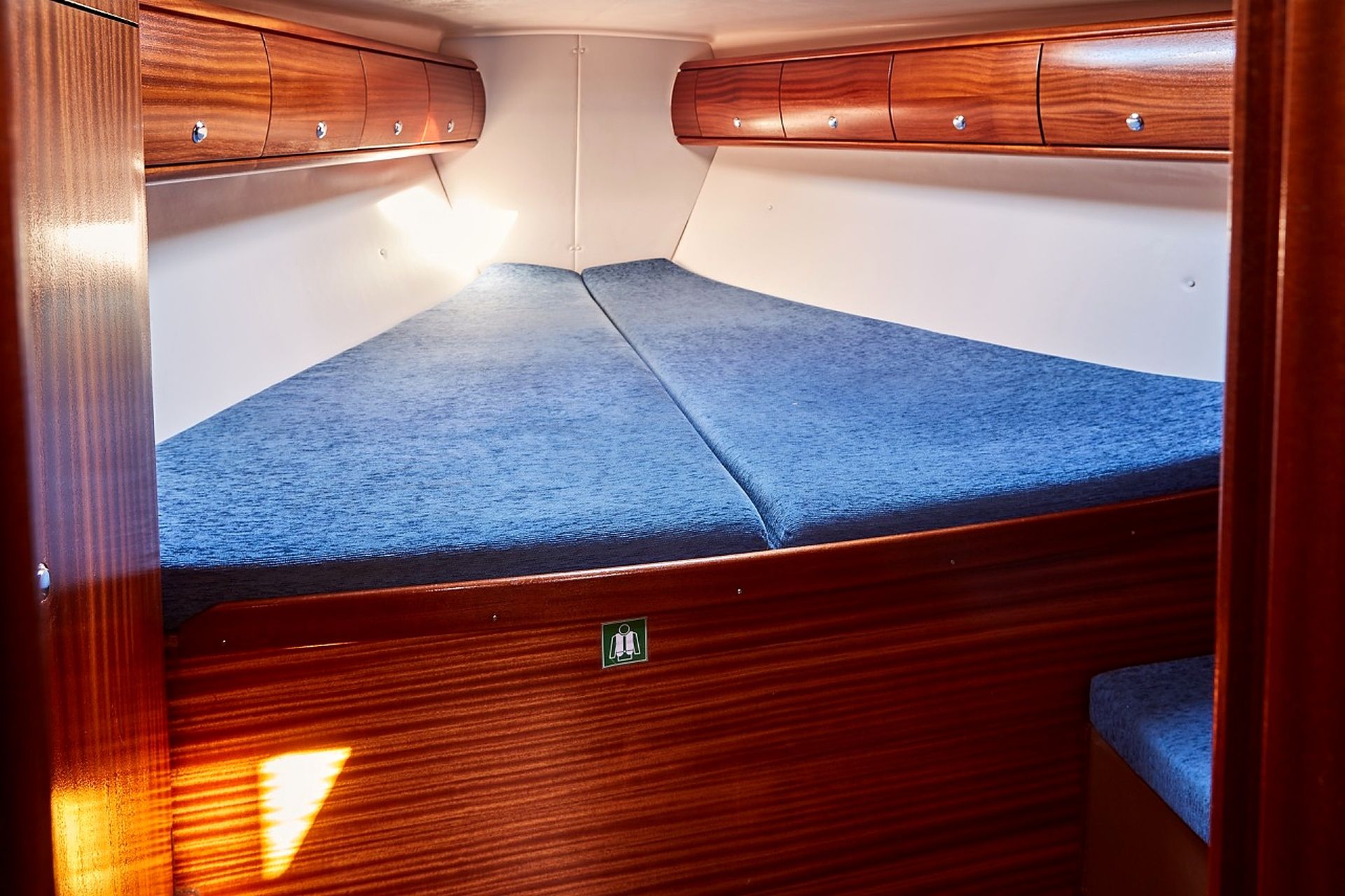 A compact interior with a blue cushioned sleeping area, wooden cabinetry, and a small green exit sign.