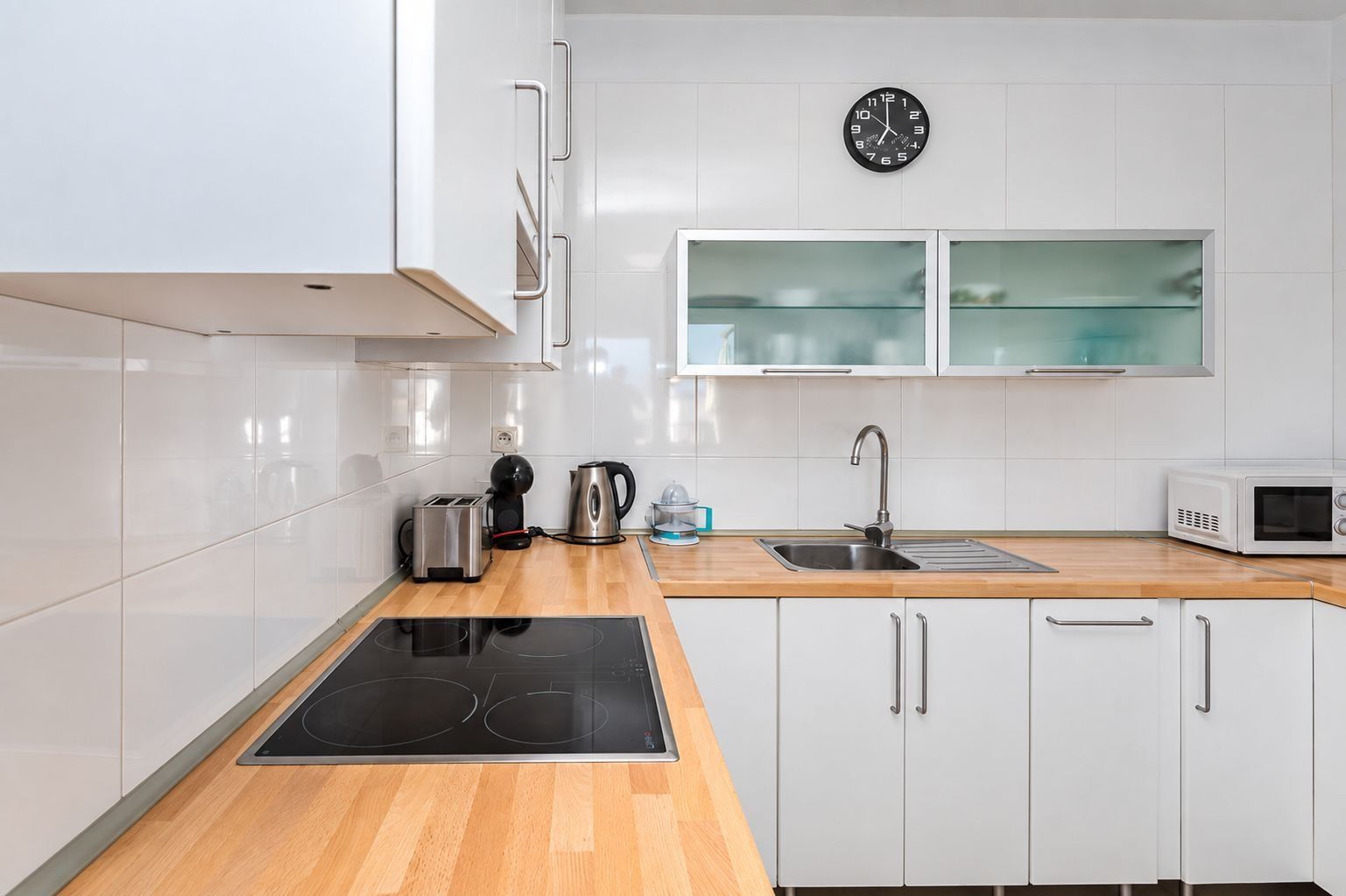 Una cocina moderna con armarios blancos, una placa de inducción negra, un hervidor de acero inoxidable, un tostador, un microondas y un lavamanos doble.