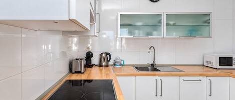 Una cucina moderna con mobili bianchi, un piano cottura a induzione nero, un bollitore in acciaio inossidabile, un tostapane, un forno a microonde e una vasca doppia.
