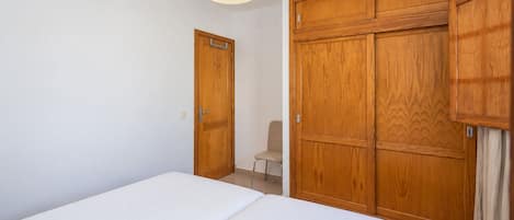 A bedroom with a bed, a wooden wardrobe, and a chair.