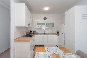 A compact kitchen with white cabinetry, a wooden countertop, a microwave, a kettle, and a dining area with a table set for two. - GuestReady - Las Tabaibas Sea View Retreat (Puerto del Carmen)