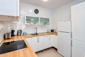 A modern kitchen with white cabinetry, a black induction cooktop, a stainless steel toaster, a kettle, a microwave, and a refrigerator. - GuestReady - Las Tabaibas Sea View Retreat (Puerto del Carmen)