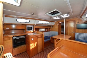 A compact kitchen with a stove, sink, and a small refrigerator. There is a seating area with a bench and a television mounted on the wall. - Sun-Kissed Sailing Adventure in Zadar, Croatia (Biograd na moru)