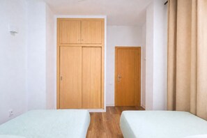 A room with two beds, wooden wardrobes, and a door. - GuestReady - Rosamar 201 P (Las Palmas de Gran Canaria)