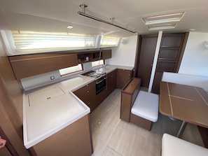 A compact kitchen with a stove, sink, and storage cabinets, a dining area with a table and chairs, and a window providing natural light.