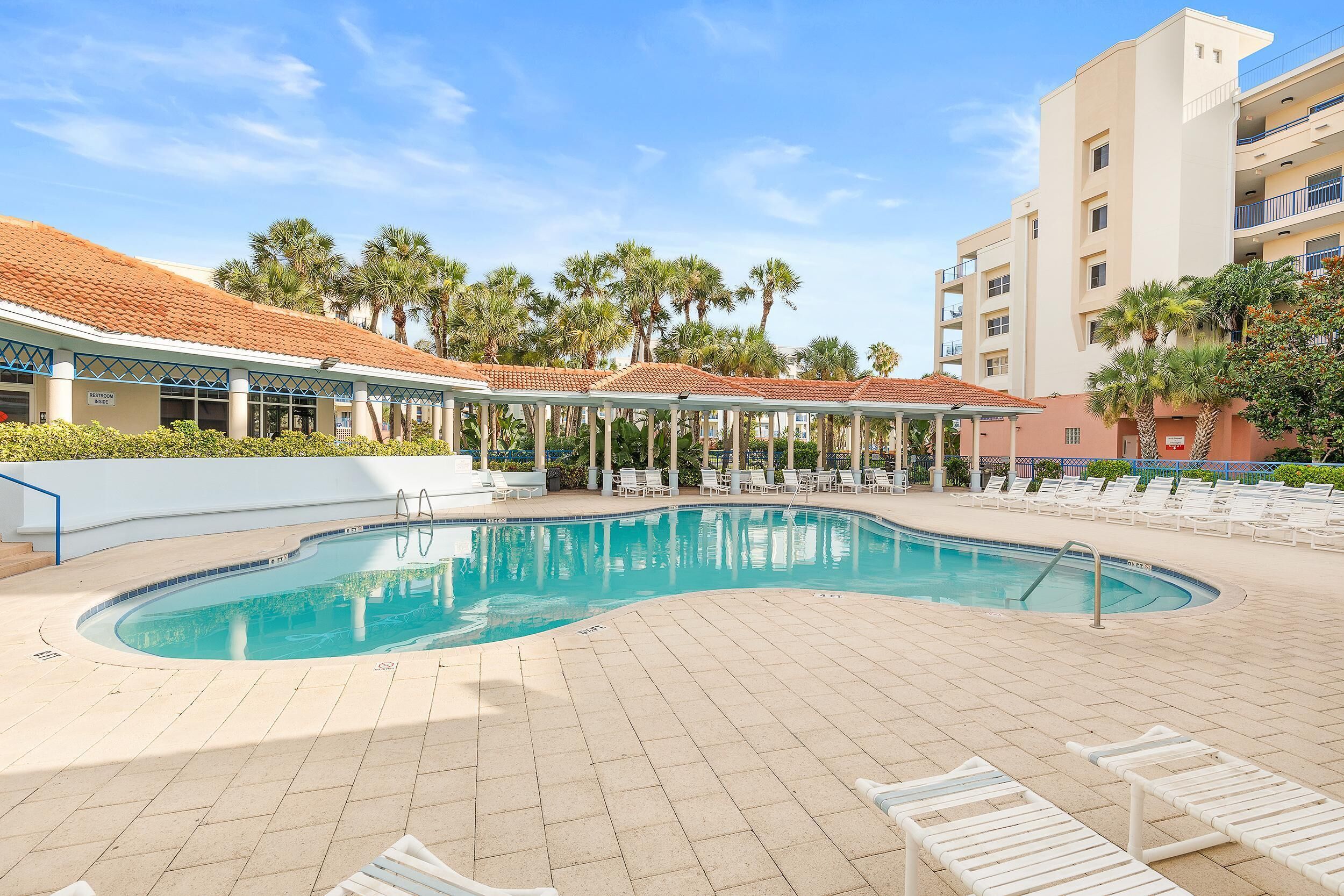 A swimming pool with lounge chairs, a covered seating area, and palm trees.