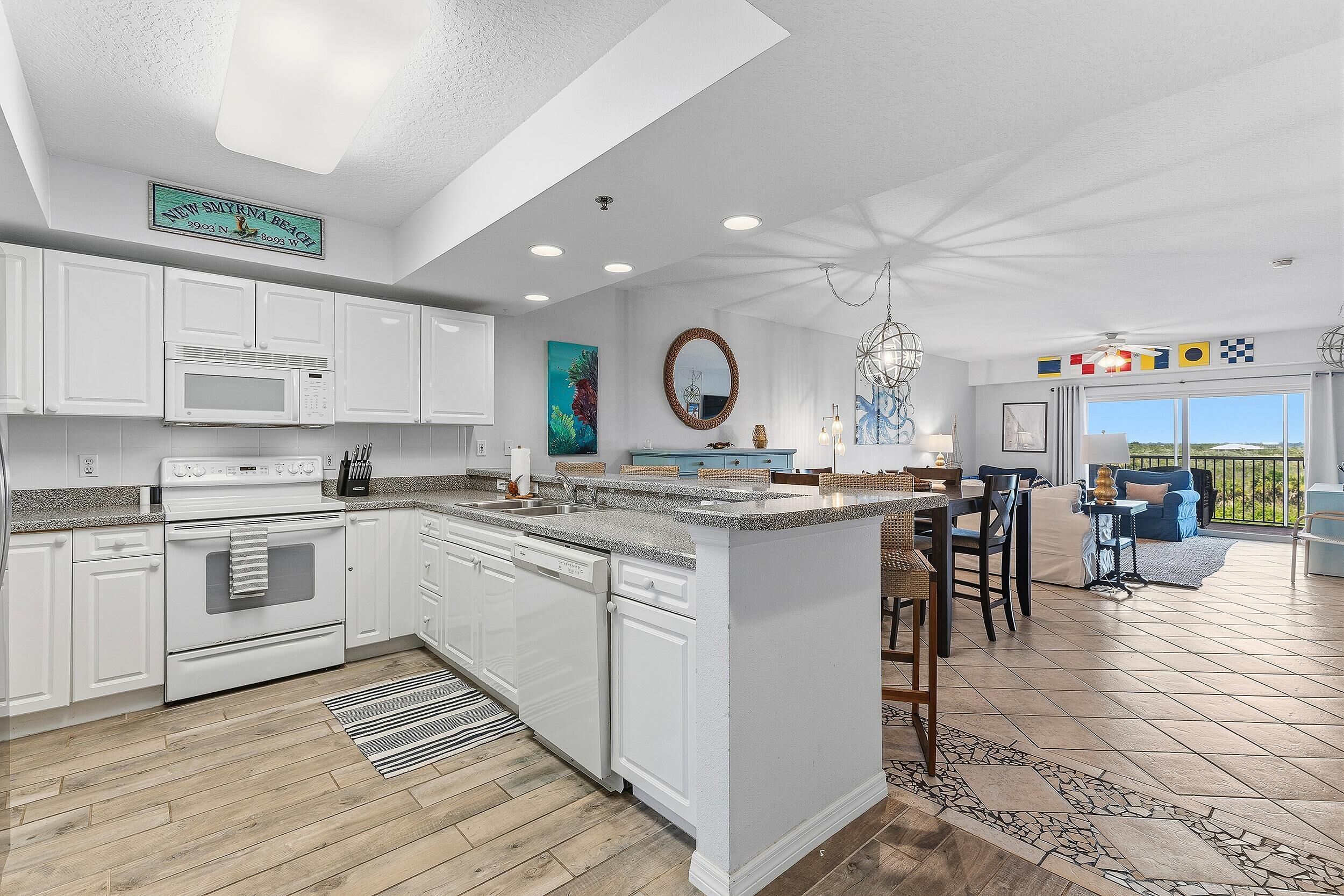 A modern kitchen with white cabinetry, a central island, and a dining area with a view.