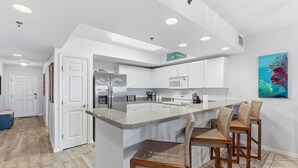A modern kitchen with white cabinets, a granite countertop, and a central island with bar stools. - Oceanwalk 4-404 (New Smyrna Beach)