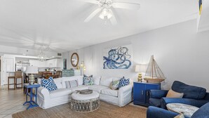 A living room with a white sofa, blue armchairs, a coffee table, and a dining area in the background. - Oceanwalk 4-404 (New Smyrna Beach)
