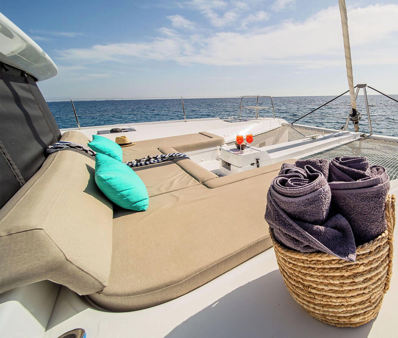 Un pont de bateau doté d’un espace salon avec des sièges rembourrés, d’un panier en osier contenant des serviettes et d’une petite table avec des verres et un chapeau.