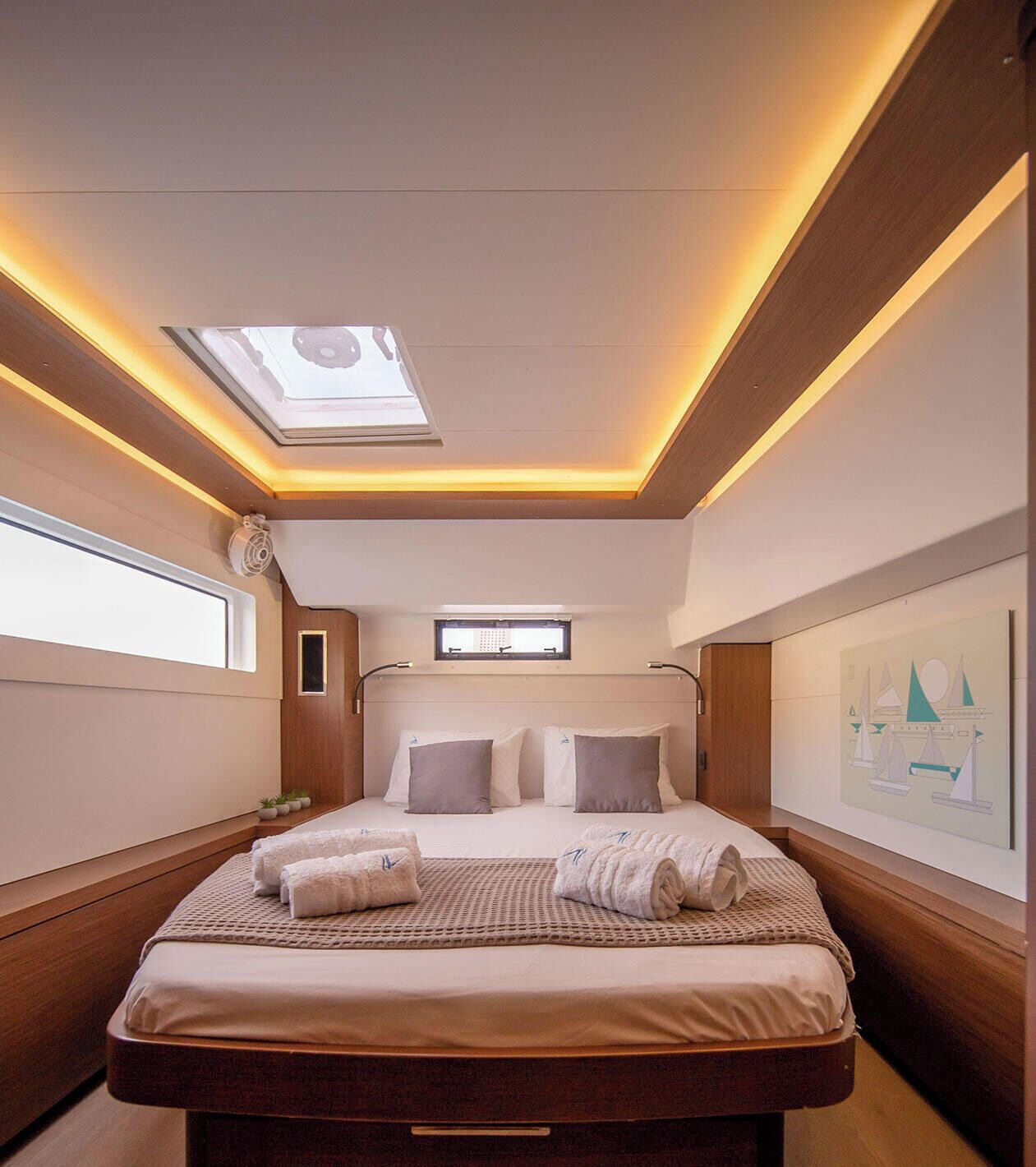A modern hotel room with a skylight, a bed with towels, a small window, and a wall art piece.