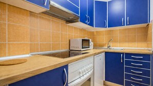 Een keuken met blauwe kastjes, een magnetron, een fornuis en een vaatwasser.