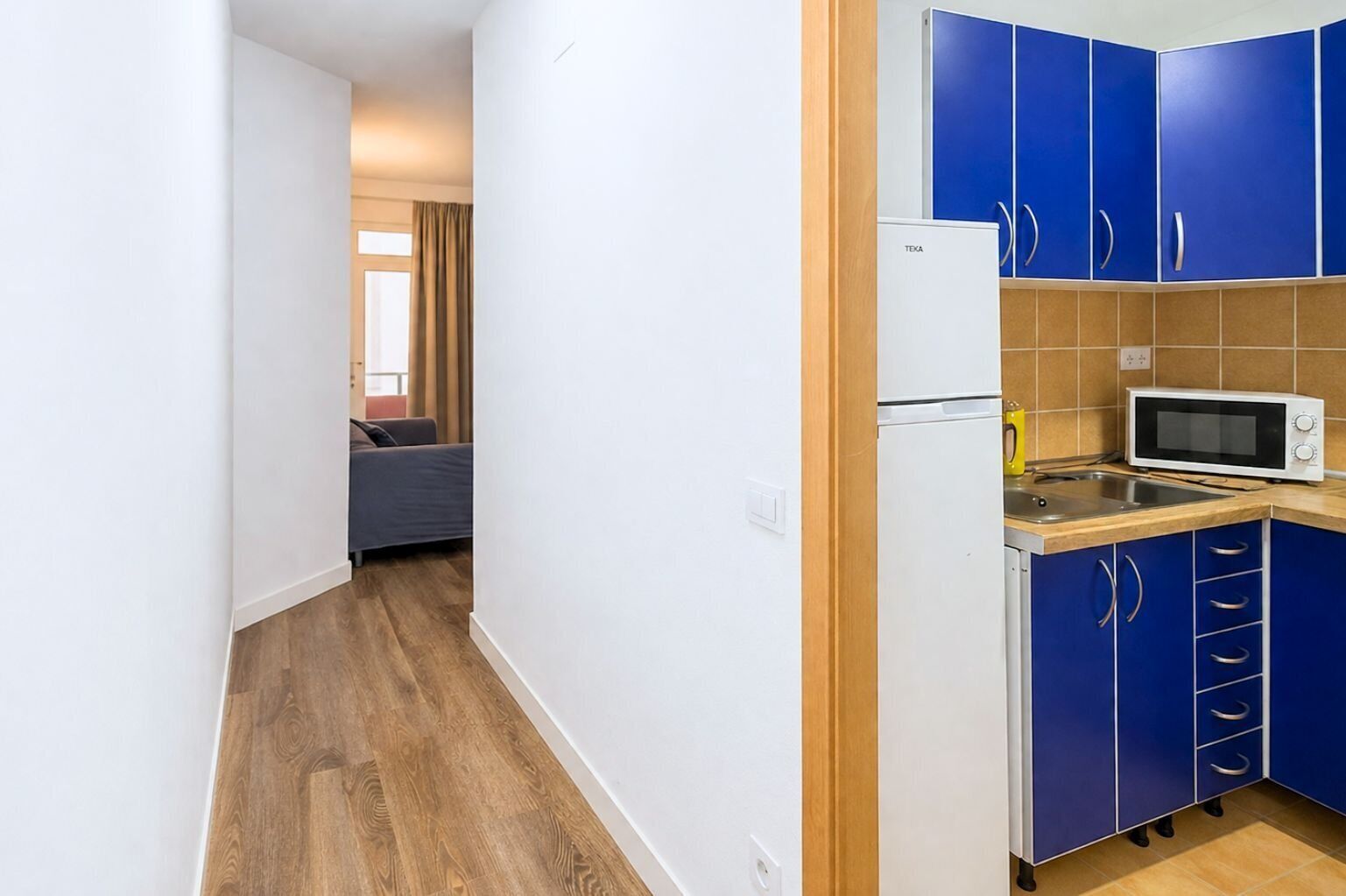 Una cocina compacta con armarios azules, un refrigerador blanco y un microondas.