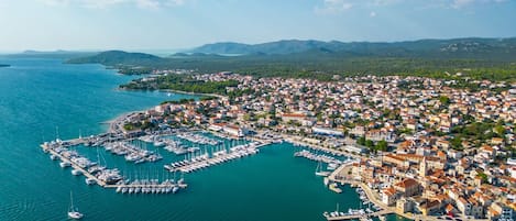 An aerial view of a coastal town with a marina, buildings, and surrounding hills.