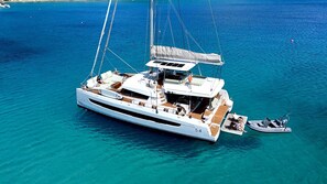 A large yacht with a covered deck and a smaller motorboat attached, floating on clear blue water.