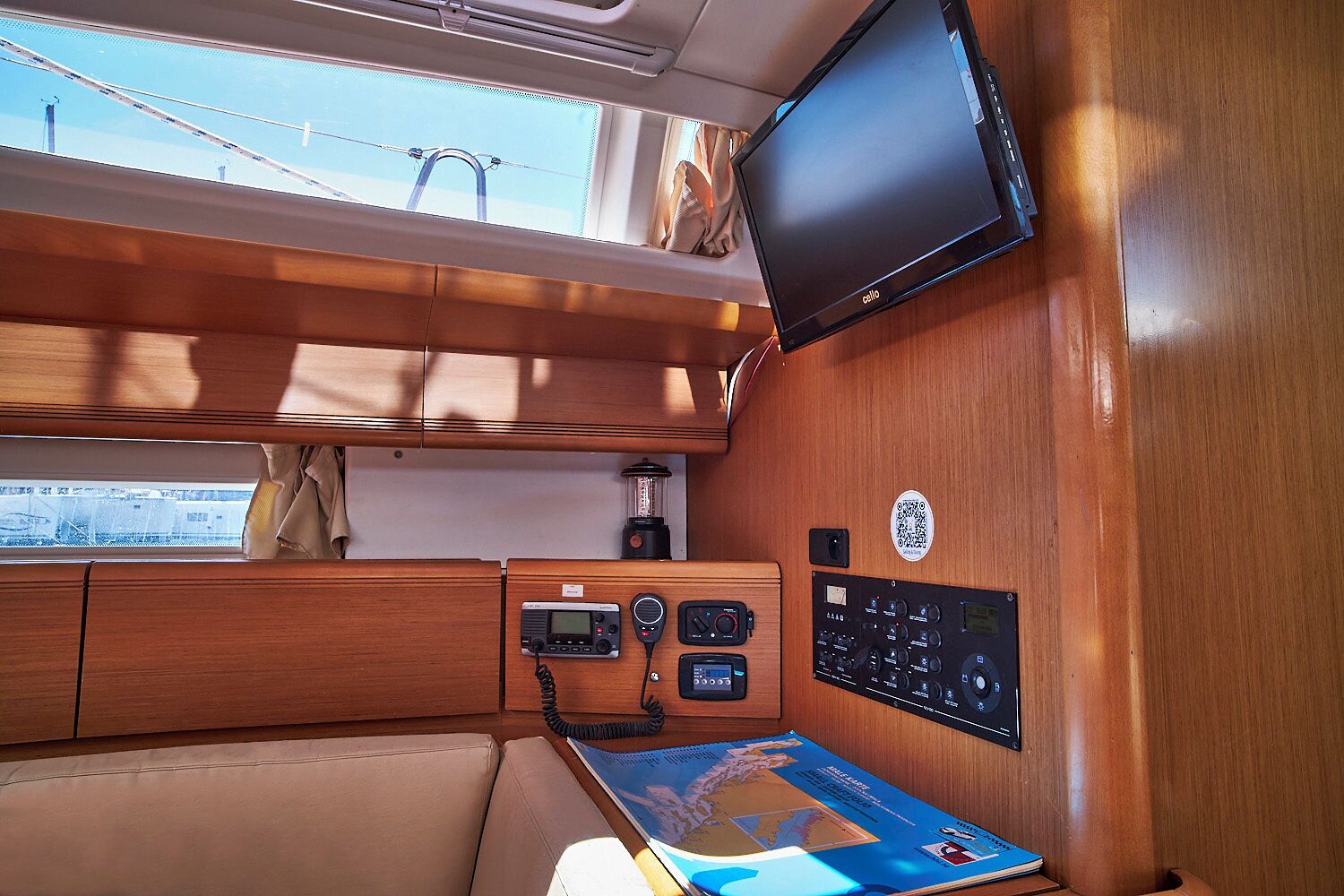 A cabin with a wooden interior, a flat-screen TV mounted on the wall, a control panel with various buttons and dials, and a map on the table.
