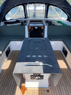 A boat's interior with a central table, seating on either side, and a view of the water through the windows.