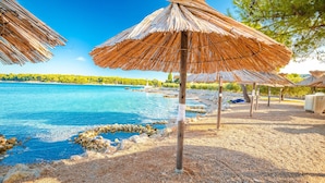 A beach with thatched umbrellas, clear blue water, and a rocky shoreline. - Sun-Kissed Sailing Adventure in Northern Croatia (Punat)