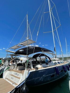 A sailboat docked at a marina with a covered deck area, a seating area labeled 'LUPELA,' and the name 'KUFNER 54' on the hull.