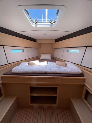 A compact, well-lit interior with a central bed, built-in storage, and a skylight.