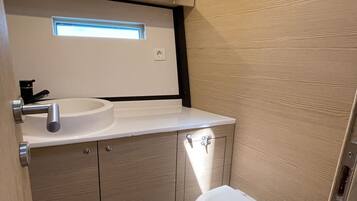 Une petite salle de bain avec un lavabo blanc, des toilettes et une petite fenêtre située au-dessus du lavabo.