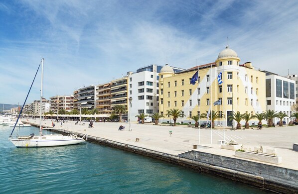 Une promenade en bord de mer bordée d’immeubles, un quai avec un voilier et des palmiers.