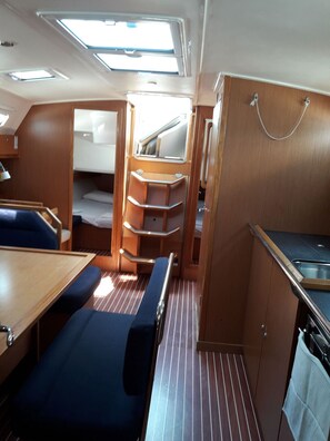 Un interior de barco compacto con comedor, pequeña cocina y una litera.