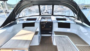 Interior de barco com uma mesa central, duas mesinhas laterais e um painel de controle.