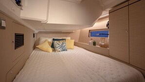 A bedroom with a bed, pillows, a shelf with bottles, and a wall-mounted TV.