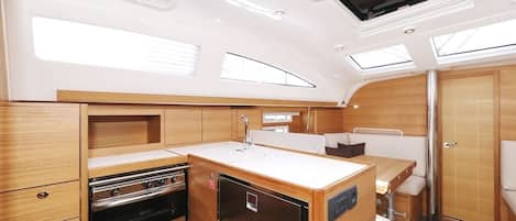 A compact galley with a stove, refrigerator, and sink, wooden cabinets, and a skylight.